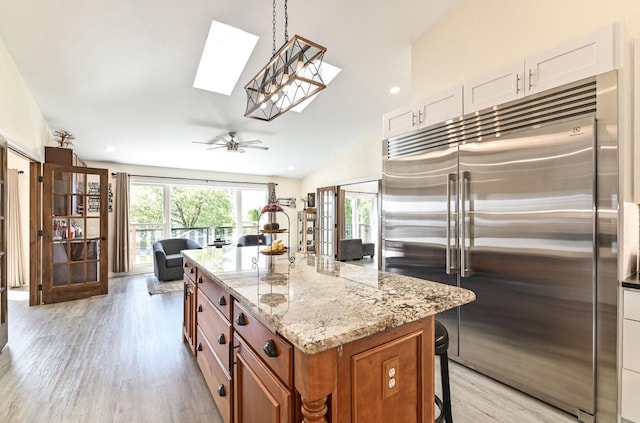 7134 N Tichigan Rd, Waterford, WI 53185 - kitchen featuring stainless steel built in refrigerator, a skylight, brown cabinetry, light wood-type flooring, and light stone counters