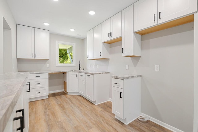 kitchen with light stone countertops, white cabinetry, sink, and light hardwood / wood-style flooring