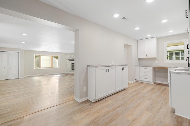 4705 Highland Park Dr, Slinger, WI 53086 - kitchen with a sink, light wood-type flooring, white cabinetry, a stone fireplace, and baseboards
