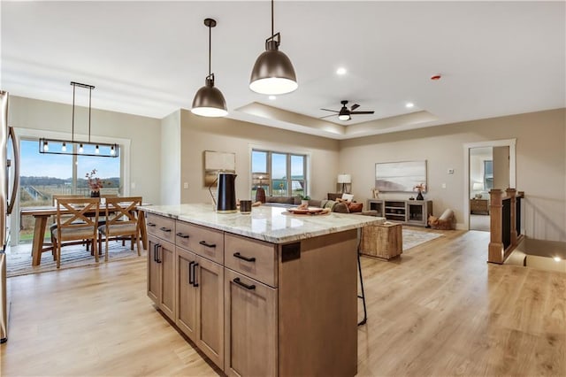 kitchen with light stone counters, pendant lighting, a tray ceiling, a kitchen island, and light wood-type flooring