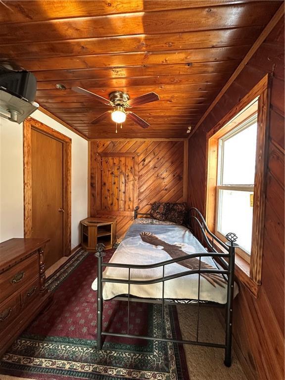 bedroom featuring ceiling fan, wood walls, and wood ceiling