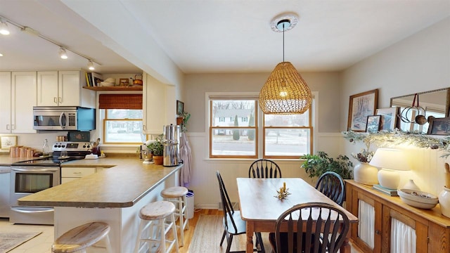 kitchen featuring light hardwood / wood-style flooring, kitchen peninsula, decorative light fixtures, a kitchen bar, and appliances with stainless steel finishes