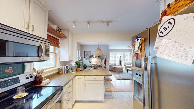 kitchen featuring white cabinetry, kitchen peninsula, pendant lighting, appliances with stainless steel finishes, and light wood-type flooring