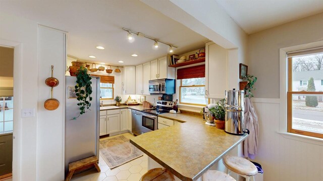 kitchen with a kitchen breakfast bar, kitchen peninsula, white cabinetry, and appliances with stainless steel finishes