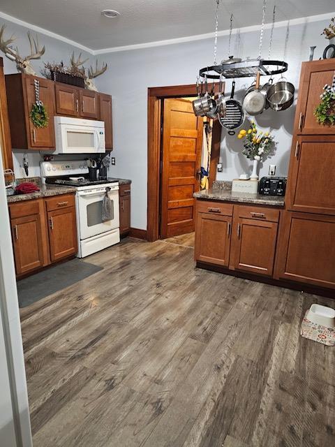 kitchen featuring crown molding, white appliances, dark wood-type flooring, and dark stone counters