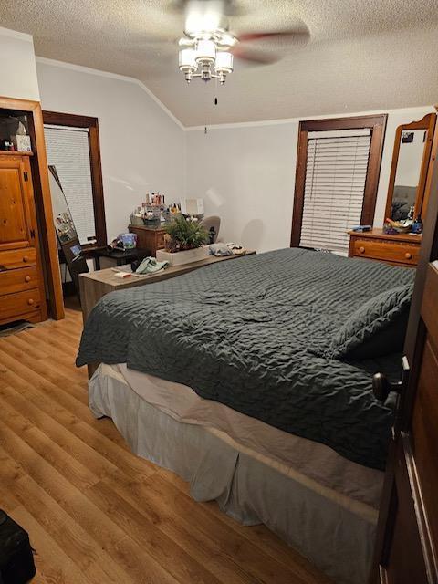 bedroom featuring lofted ceiling, ceiling fan, light wood-type flooring, a textured ceiling, and ornamental molding