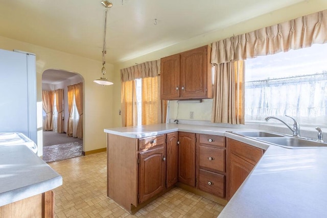 kitchen with decorative light fixtures, white refrigerator, kitchen peninsula, and sink