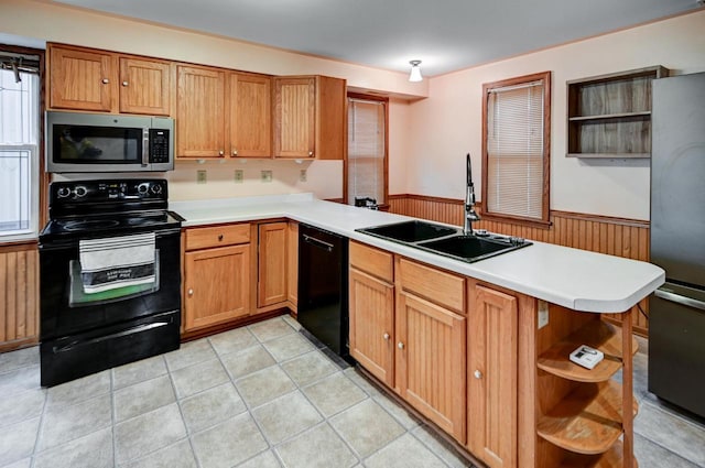 kitchen with kitchen peninsula, sink, black appliances, light tile patterned floors, and wood walls