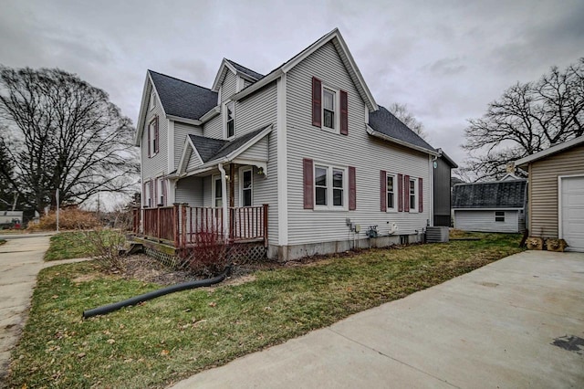 view of property exterior with a yard, covered porch, central AC unit, a garage, and an outbuilding