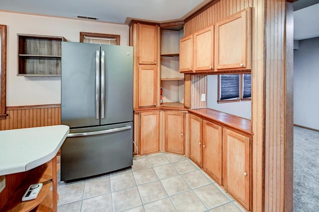 kitchen with light carpet, stainless steel refrigerator, and wood walls