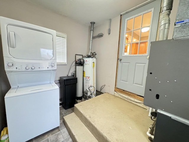 clothes washing area with tile patterned floors, stacked washer / drying machine, and water heater