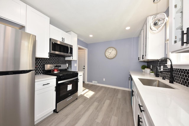 kitchen featuring white cabinets, sink, hanging light fixtures, light hardwood / wood-style floors, and stainless steel appliances