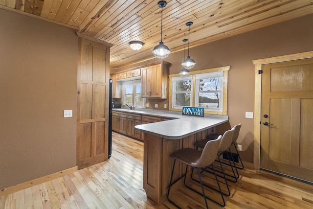 kitchen featuring light hardwood / wood-style flooring, kitchen peninsula, pendant lighting, a breakfast bar area, and wood ceiling