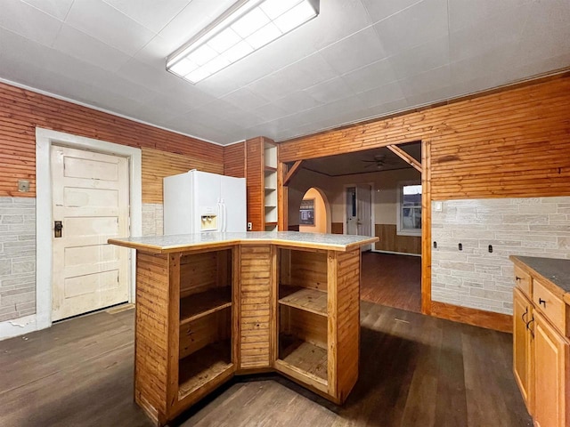 kitchen featuring wood walls, dark hardwood / wood-style floors, ceiling fan, white fridge with ice dispenser, and a kitchen island