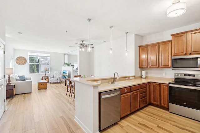 kitchen featuring light wood-type flooring, kitchen peninsula, sink, and appliances with stainless steel finishes