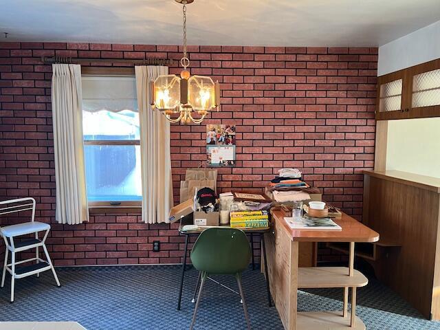 carpeted dining room featuring a notable chandelier and brick wall