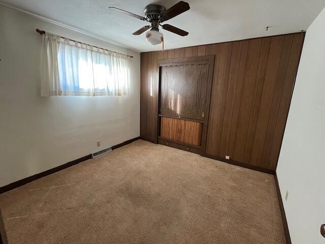 unfurnished bedroom with ceiling fan, light colored carpet, and wooden walls