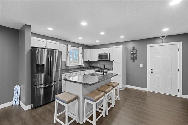 kitchen featuring a center island with sink, white cabinets, appliances with stainless steel finishes, dark hardwood / wood-style flooring, and a breakfast bar area