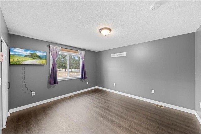 unfurnished room with a textured ceiling and dark wood-type flooring