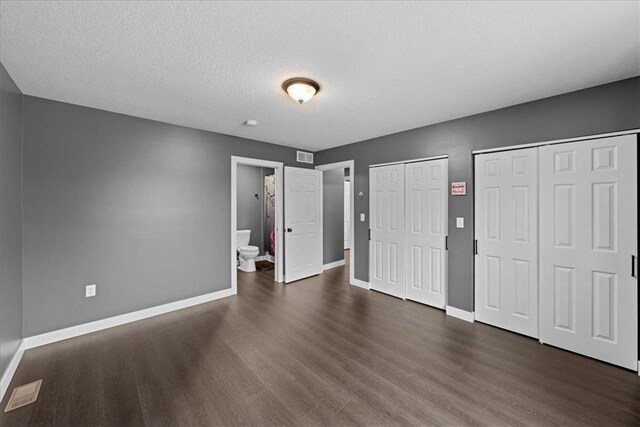 interior space featuring a textured ceiling, two closets, ensuite bathroom, and dark hardwood / wood-style floors