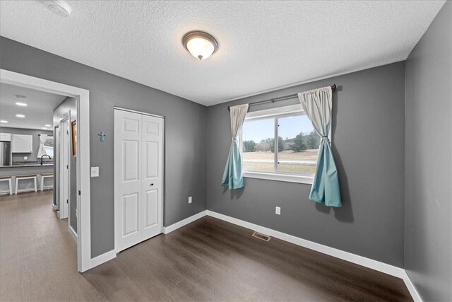 unfurnished room featuring a textured ceiling, dark wood-type flooring, and sink