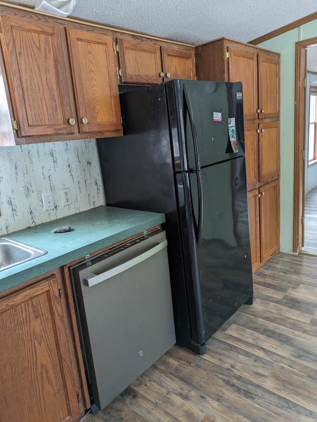 kitchen featuring dark wood-type flooring, black fridge, stainless steel dishwasher, a textured ceiling, and ornamental molding