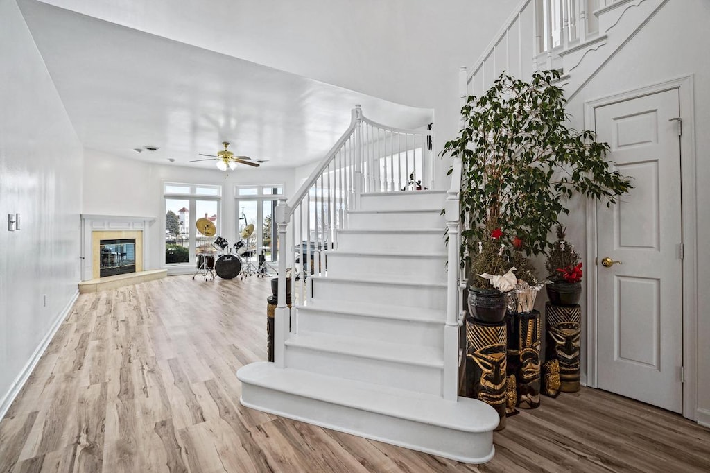 staircase featuring ceiling fan, wood-type flooring, and a high end fireplace