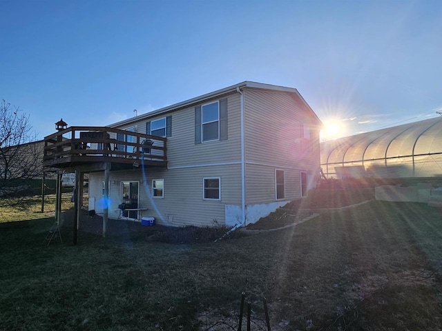 back house at dusk with a wooden deck and a yard