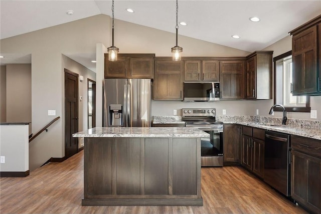 kitchen featuring stainless steel appliances, a kitchen island, hanging light fixtures, and light stone counters