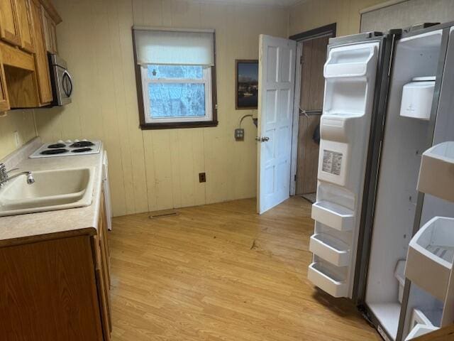 kitchen with wood walls, white gas stovetop, sink, light wood-type flooring, and fridge