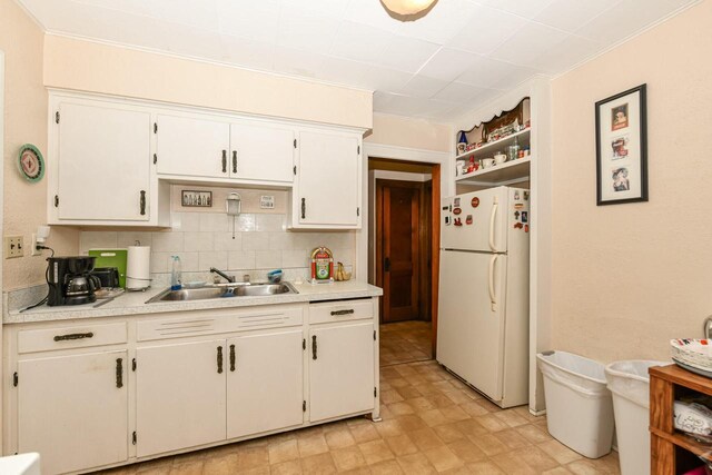 kitchen with white cabinets, white refrigerator, sink, ornamental molding, and tasteful backsplash