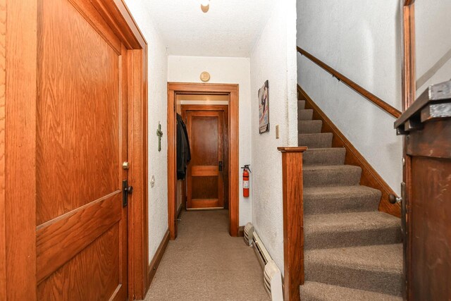 staircase with a textured ceiling, baseboard heating, and carpet