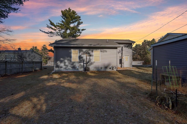 back house at dusk featuring a lawn