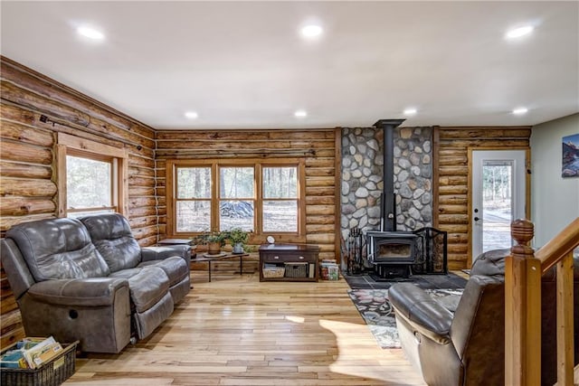 living room featuring log walls, light hardwood / wood-style flooring, a wood stove, and plenty of natural light