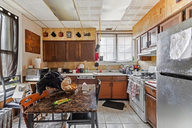 kitchen featuring light tile patterned floors, white gas range oven, stainless steel refrigerator, and sink