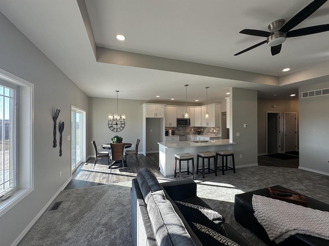 living room featuring dark colored carpet and ceiling fan with notable chandelier