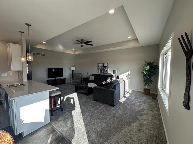 living room with a raised ceiling, dark carpet, and ceiling fan