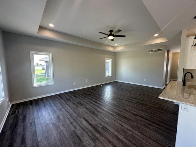 unfurnished living room featuring a raised ceiling, dark wood-type flooring, and sink