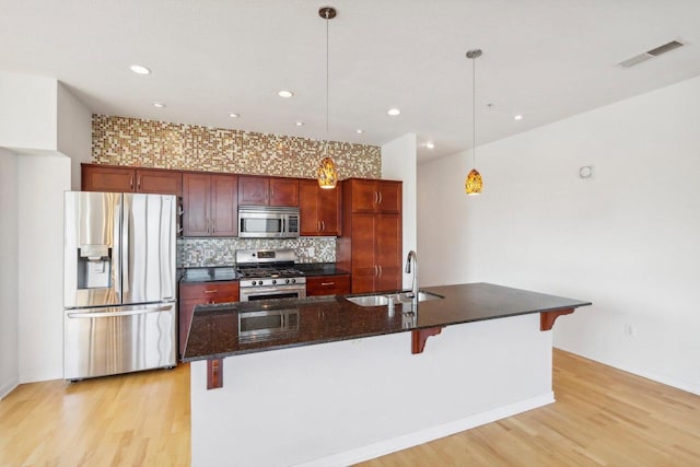 kitchen with sink, hanging light fixtures, stainless steel appliances, light hardwood / wood-style flooring, and a kitchen island with sink