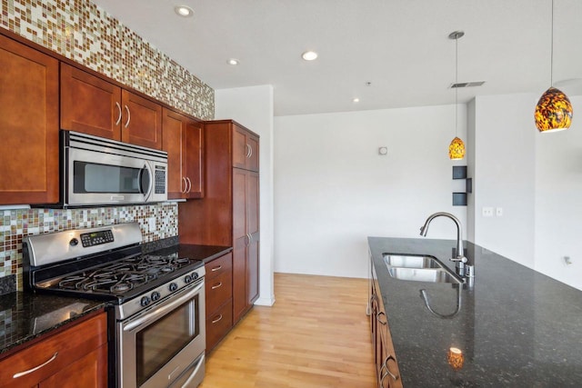 kitchen featuring appliances with stainless steel finishes, hanging light fixtures, dark stone countertops, and sink