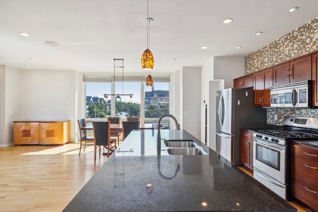 kitchen featuring sink, dark stone counters, decorative light fixtures, appliances with stainless steel finishes, and light wood-type flooring