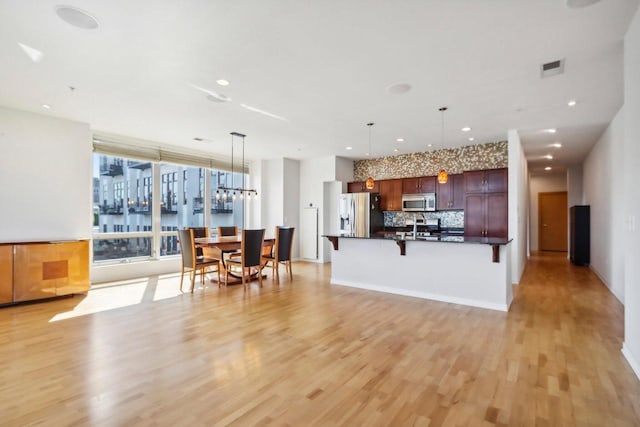 kitchen with decorative backsplash, appliances with stainless steel finishes, light wood-type flooring, a kitchen bar, and hanging light fixtures