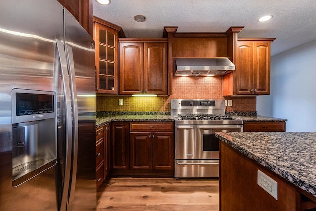 kitchen featuring light hardwood / wood-style flooring, decorative backsplash, dark stone countertops, range hood, and appliances with stainless steel finishes