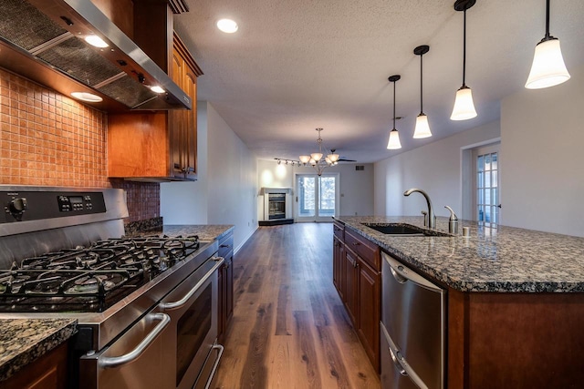 kitchen featuring appliances with stainless steel finishes, sink, wall chimney range hood, pendant lighting, and a center island with sink