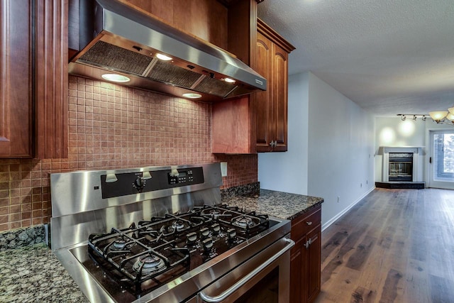 kitchen featuring wall chimney exhaust hood, dark hardwood / wood-style floors, stainless steel range with gas cooktop, and dark stone counters