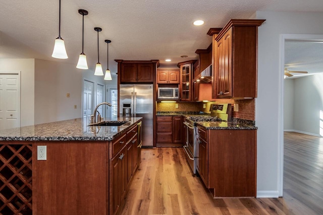 kitchen with sink, stainless steel appliances, an island with sink, light hardwood / wood-style floors, and decorative light fixtures