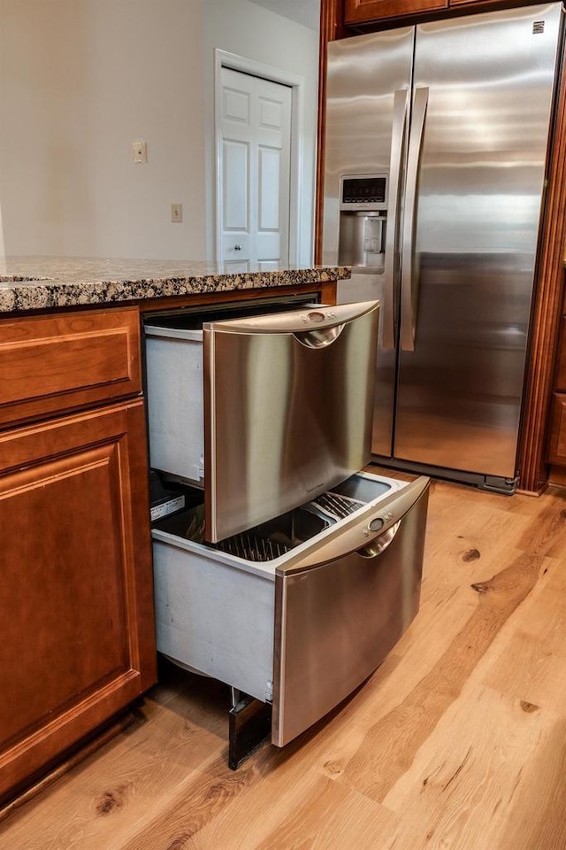 kitchen featuring light stone countertops, stainless steel refrigerator with ice dispenser, and light hardwood / wood-style flooring