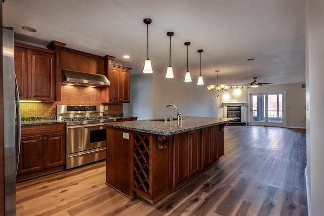 kitchen featuring hardwood / wood-style floors, appliances with stainless steel finishes, a kitchen island with sink, and wall chimney range hood