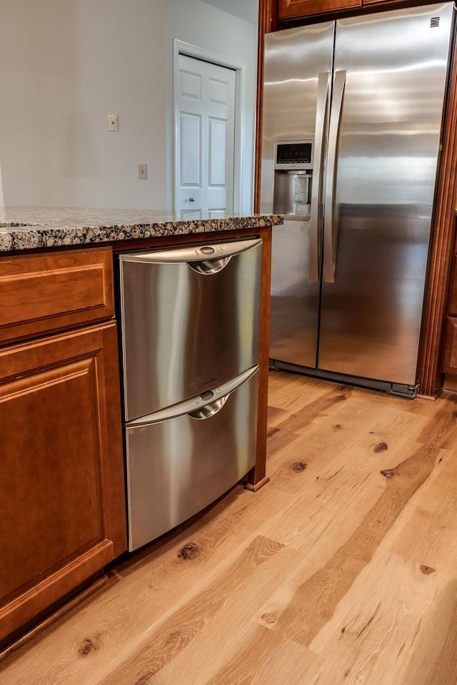 kitchen with stone countertops, appliances with stainless steel finishes, and light hardwood / wood-style flooring