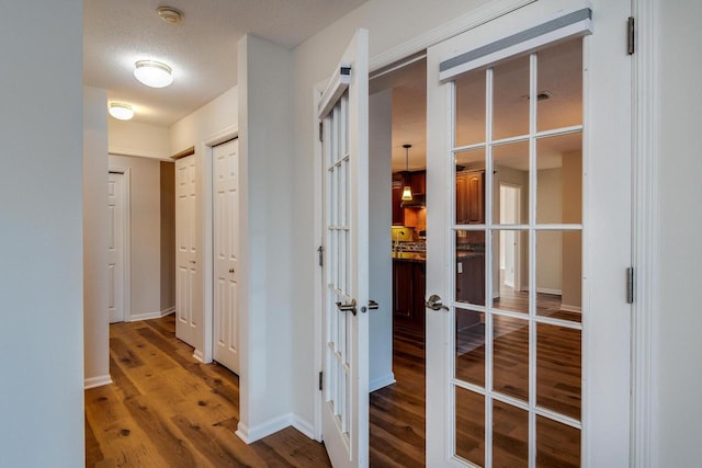 corridor with wood-type flooring, a textured ceiling, and french doors